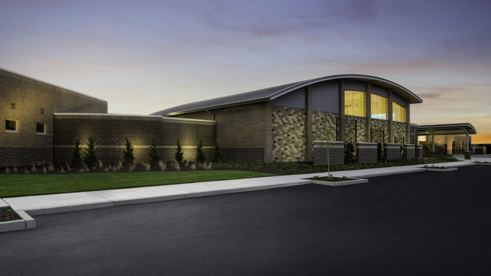 Modern brick building with a curved roof at sunset, beside a paved road and landscaped lawn