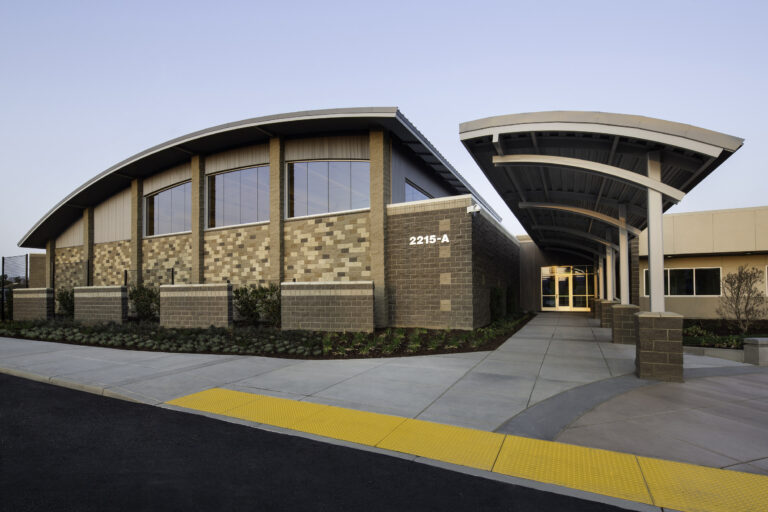 Modern brick-and-metal building entrance with curved canopy, sidewalk, and address number 2215-A