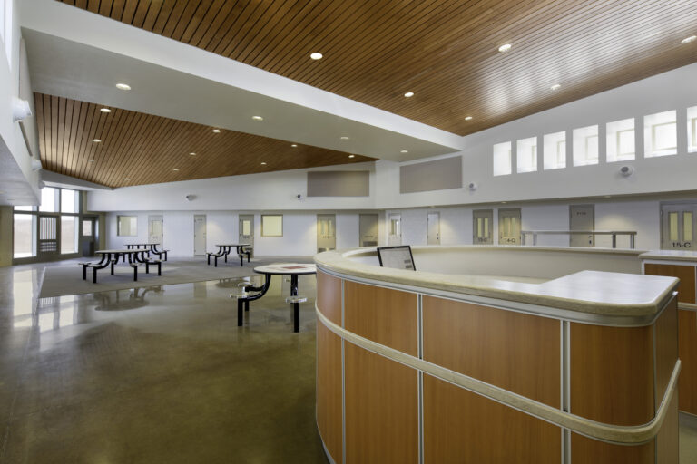 Empty modern lobby with curved reception desk, picnic tables, and a wood-paneled ceiling