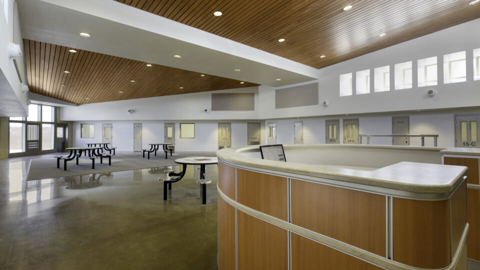 Empty modern lobby with curved reception desk, picnic tables, and a wood-paneled ceiling