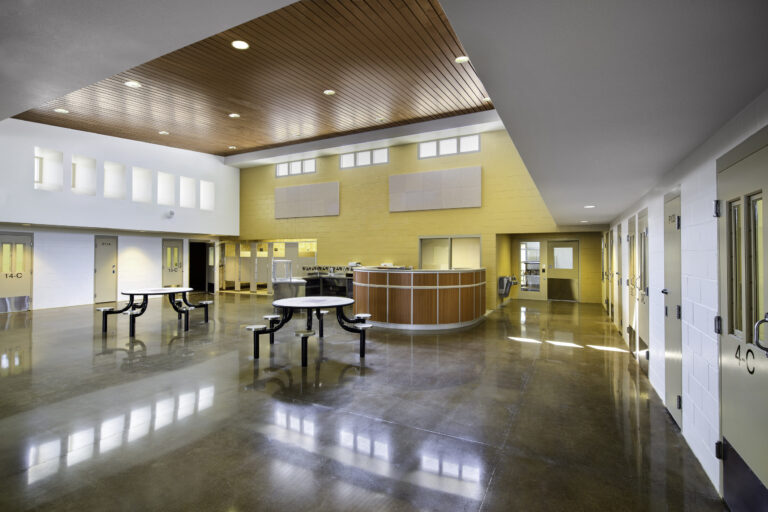 Empty modern school cafeteria with shiny floors, round tables, serving counter, and classroom doors along the walls
