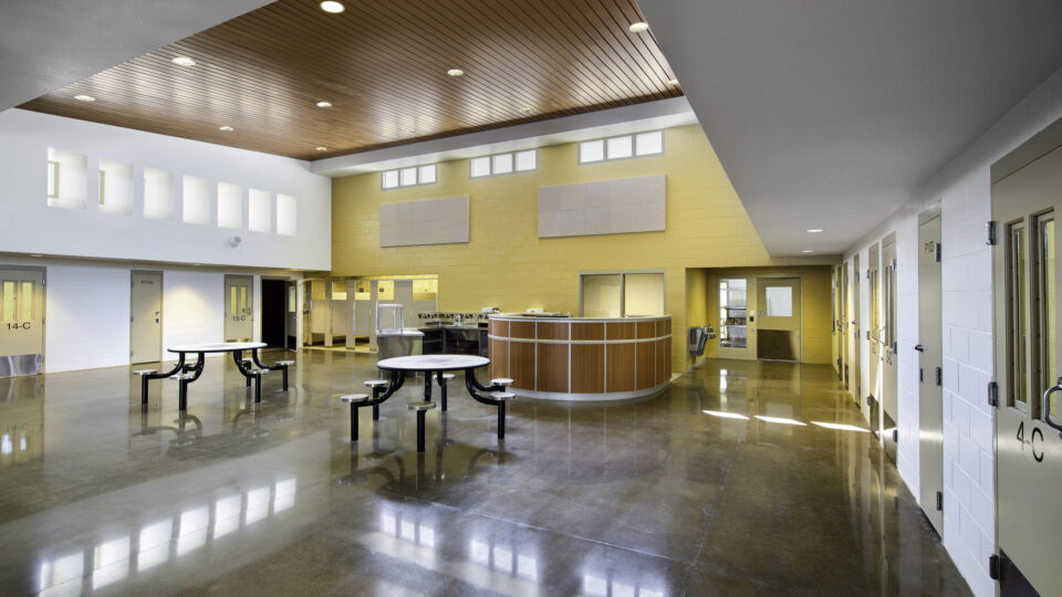 Empty modern school cafeteria with shiny floors, round tables, serving counter, and classroom doors along the walls
