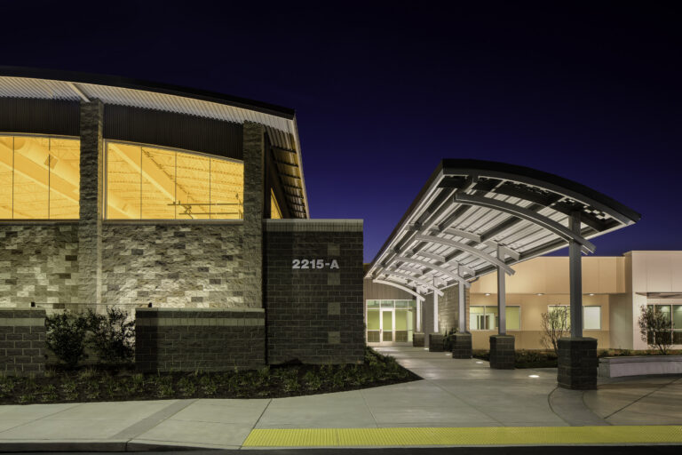 Modern building entrance at night with a curved canopy and illuminated windows, address 2215-A visible on the wall