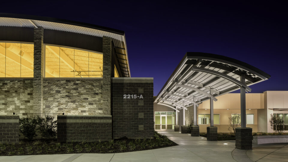 Modern building entrance at night with a curved canopy and illuminated windows, address 2215-A visible on the wall