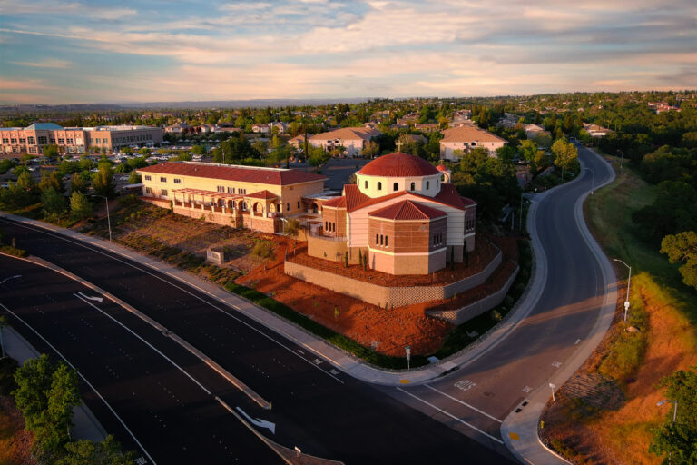 Aerial view of a suburban neighborhood with a domed church beside curving roads at sunset