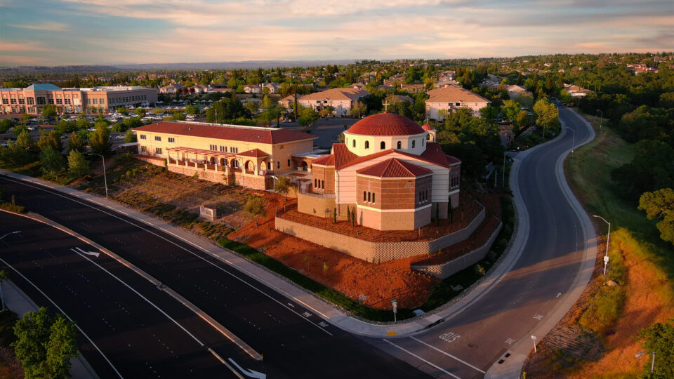 Aerial view of a suburban neighborhood with a domed church beside curving roads at sunset