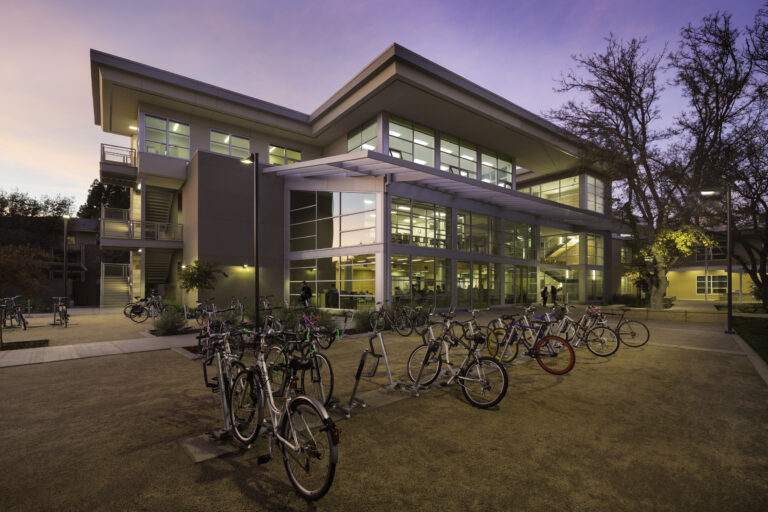 Modern campus building at dusk with many bicycles parked outside and lit windows inside