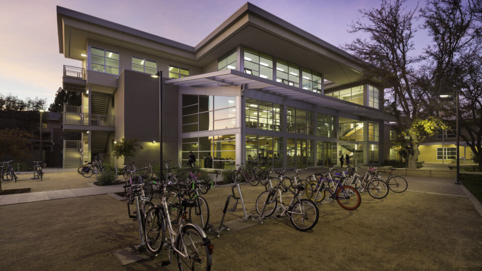 Modern campus building at dusk with many bicycles parked outside and lit windows inside