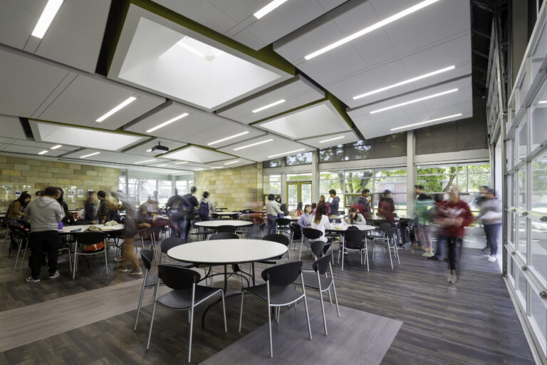 Bright modern student cafeteria with people gathered around round tables and large windows