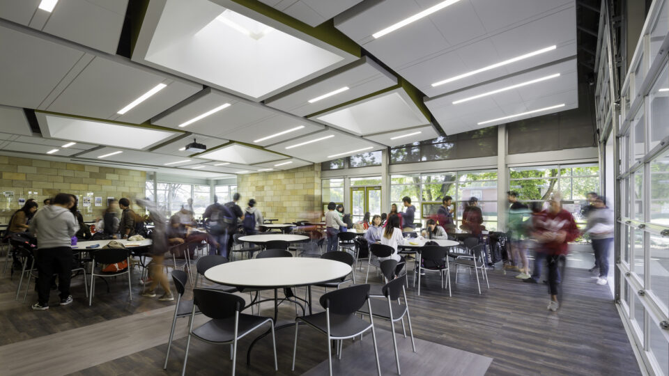 Bright modern student cafeteria with people gathered around round tables and large windows