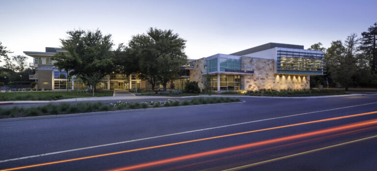 Modern campus building labeled International Center at dusk, with trees and car light trails in front