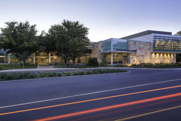 Modern campus building labeled International Center at dusk, with trees and car light trails in front