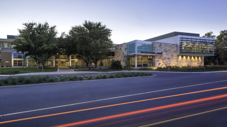 Modern campus building labeled International Center at dusk, with trees and car light trails in front