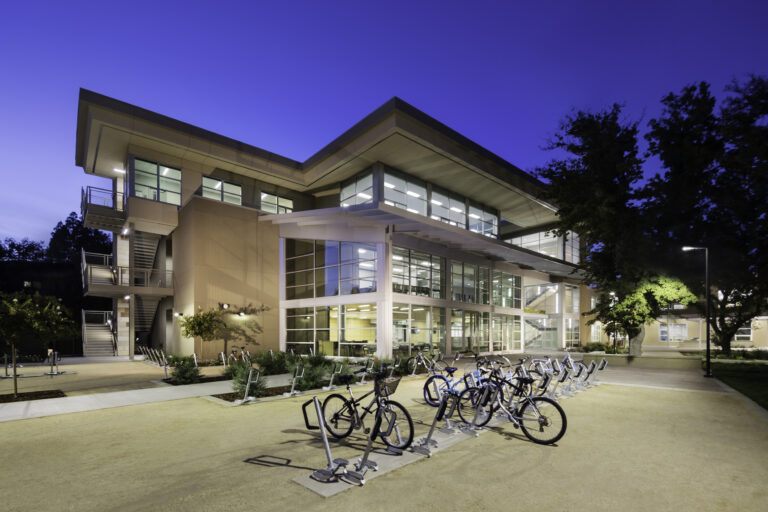 Modern campus building at dusk with lit windows and bicycles parked outside