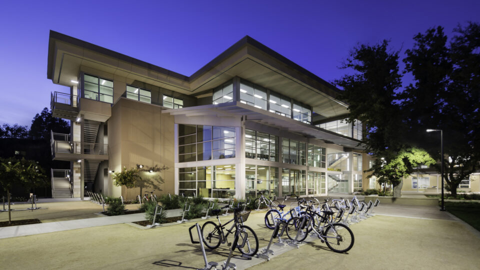 Modern campus building at dusk with lit windows and bicycles parked outside